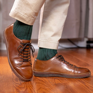 man taking a step wearing forest green ribbed dress socks with light khaki trousers and brown leather dress sneakers