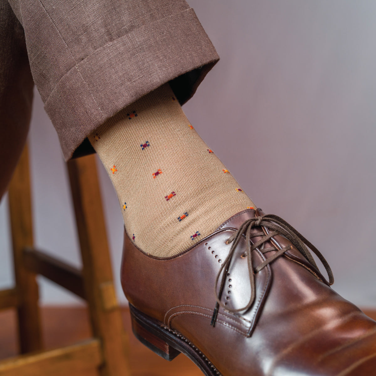 man sitting crossing his legs wearing brown slacks and khaki geometric pattern mid calf cotton dress socks