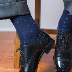 man sitting on a stool with his feet propped up wearing black oxfords and navy cotton dress socks with a geometric pattern
