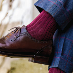 close up image of a man crossing his legs wearing plaid pants, nice shoes, and burgandy wool over the calf dress socks