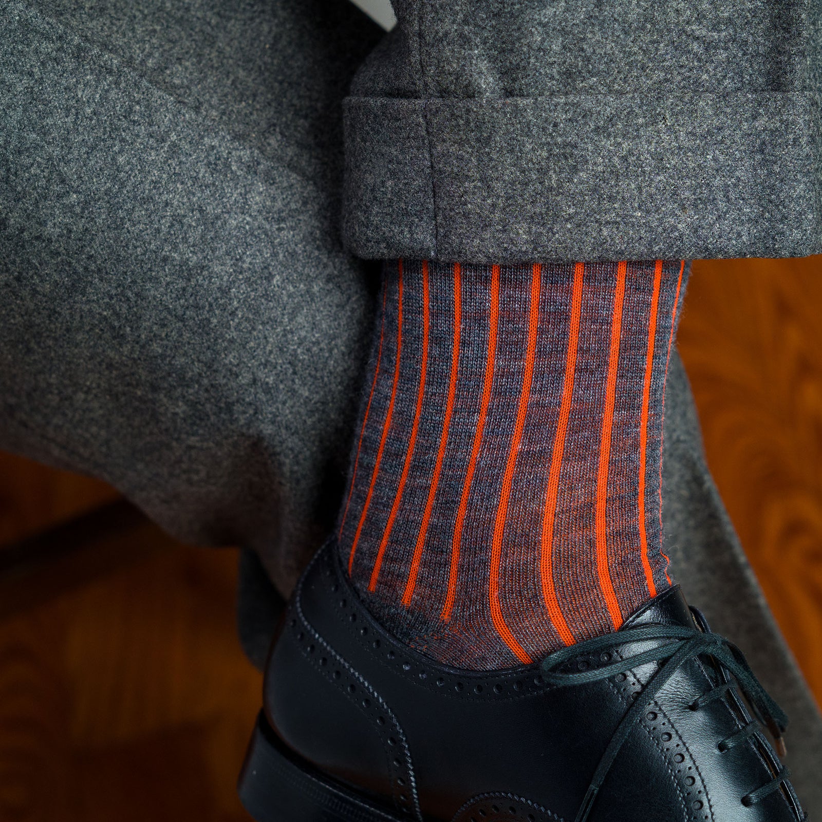 man crossing legs wearing orange and grey shadow stripe dress socks with grey slacks and black oxfords