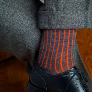 man crossing legs wearing orange and grey shadow stripe dress socks with grey slacks and black oxfords