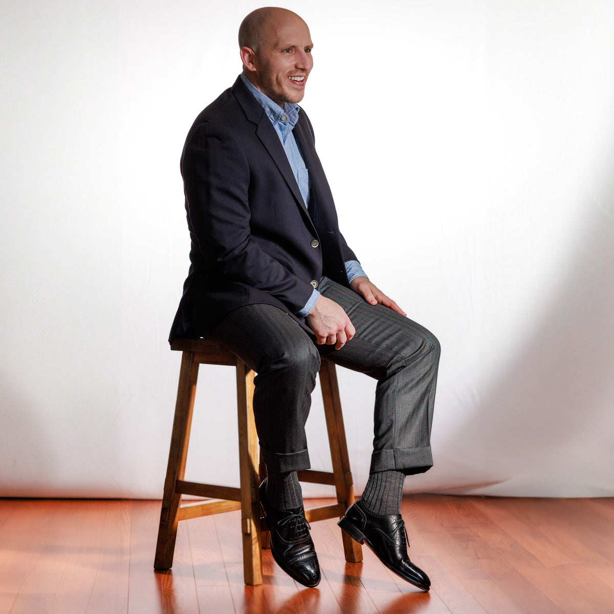 man seated on stool wearing grey heather merino wool dress socks with business attire