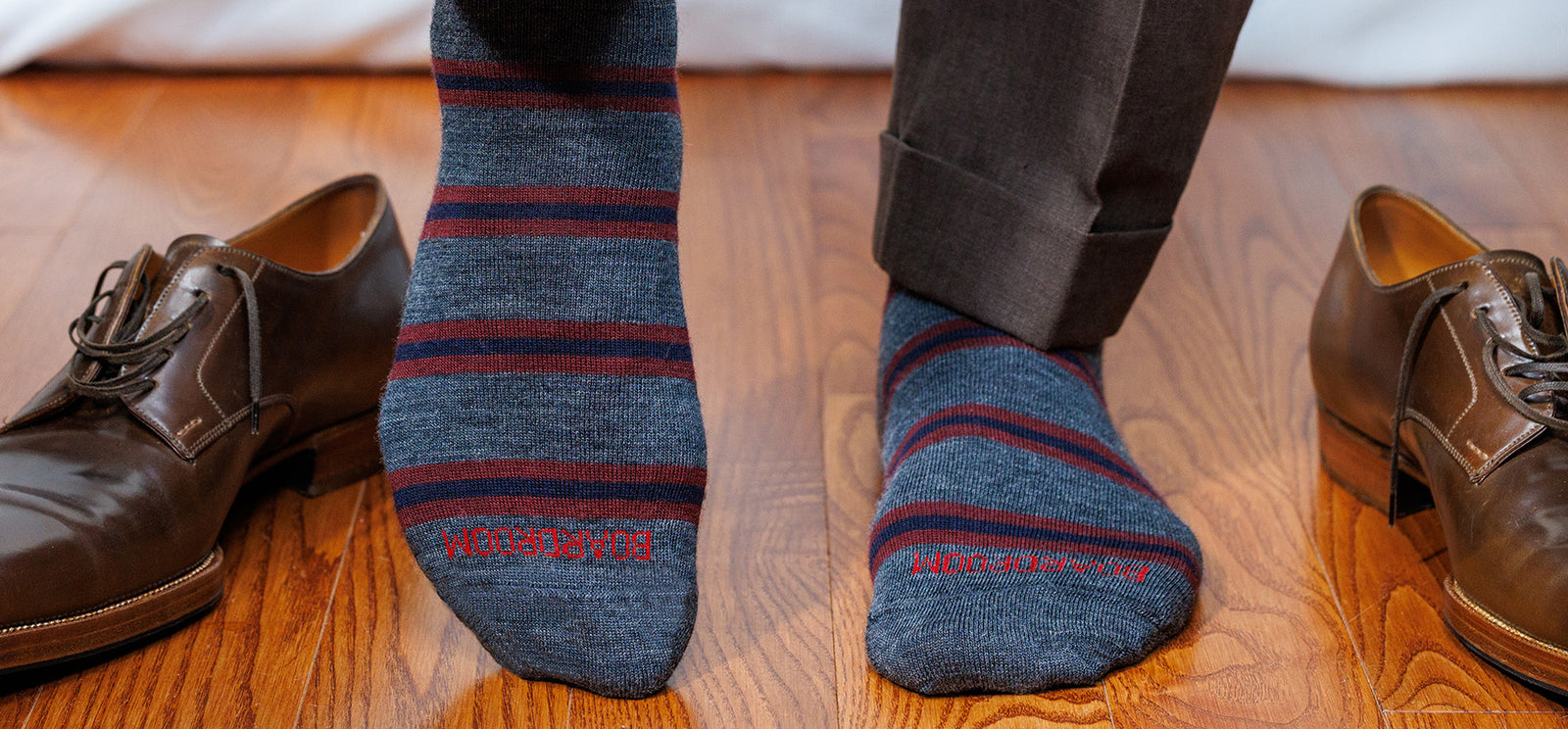 grey merino wool dress socks decorated with horizontal burgundy and navy stripes worn by man standing on hardwood floor