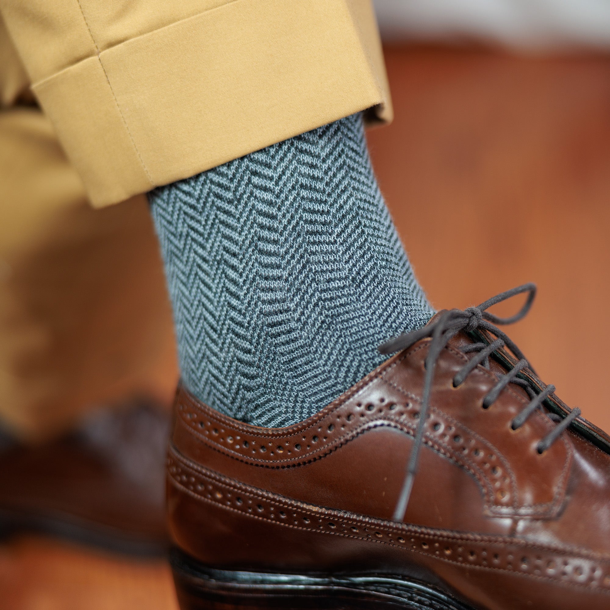 man wearing grey herringbone dress socks with khaki slacks and brown wingtips crossing legs