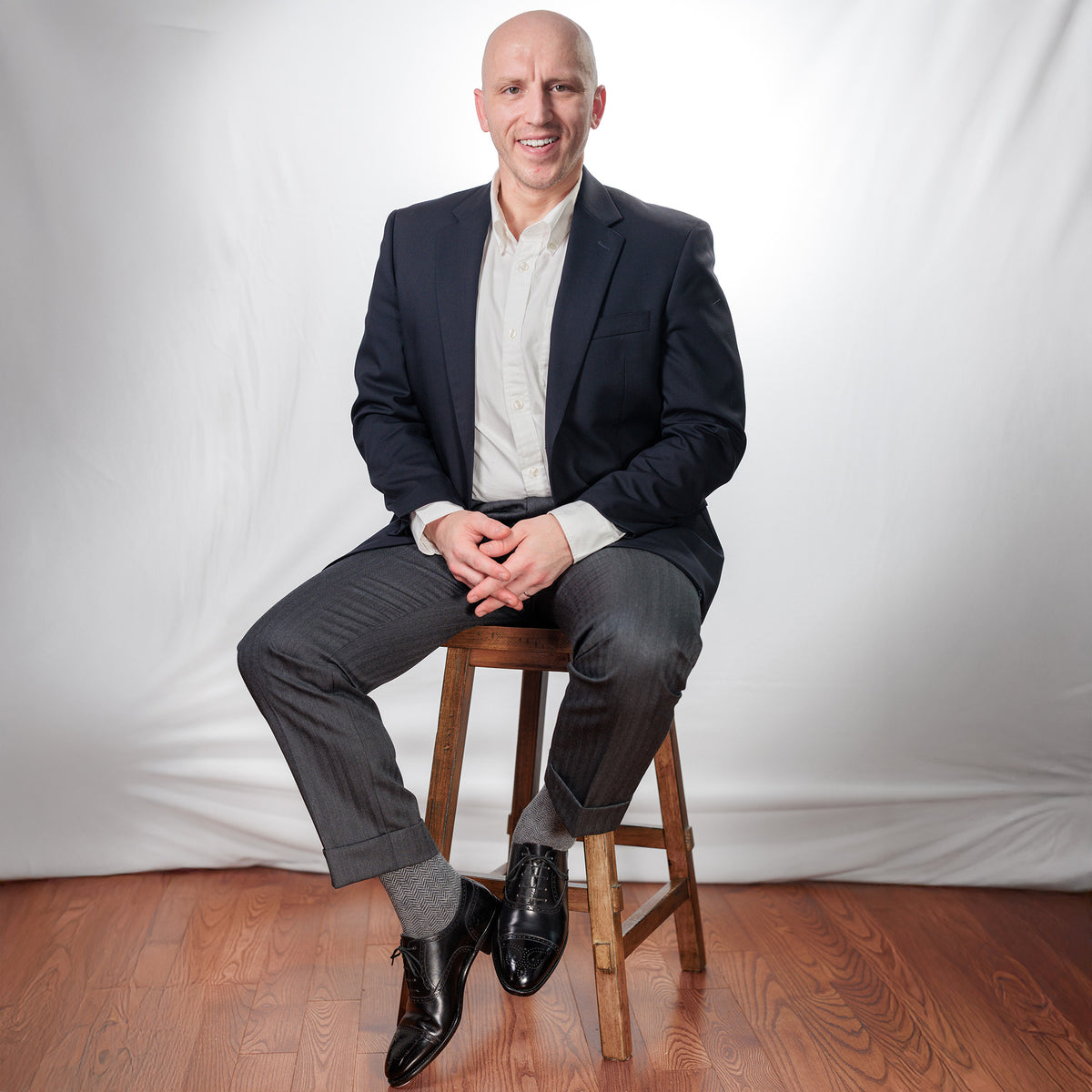 man wearing business casual attire with grey herringbone dress socks sitting on stool