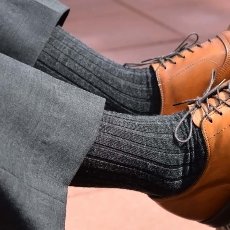 man wearing grey ribbed dress socks with a grey suit and light brown dress shoes with his feet propped up