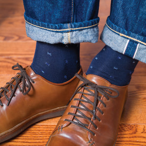 man standing on hardwood floors wearing brown shoes and navy over the calf geometric pattern dress socks