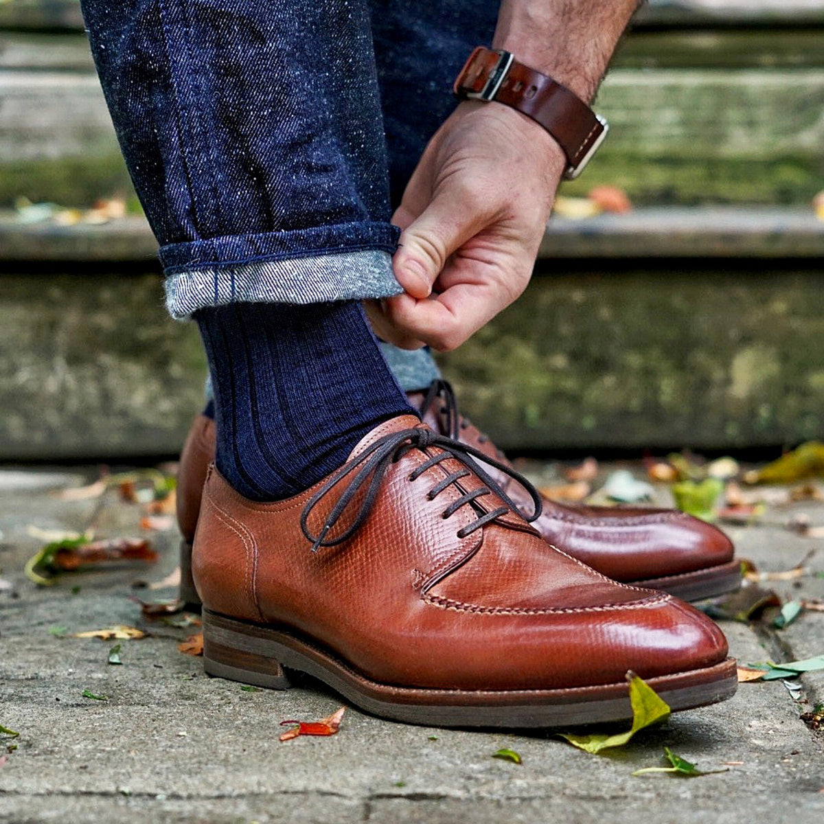 man bending down to straighten the hem of his jeans while wearing navy wool dress socks