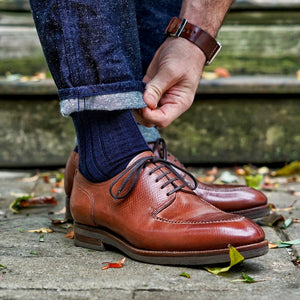 man bending down to straighten the hem of his jeans while wearing navy wool dress socks