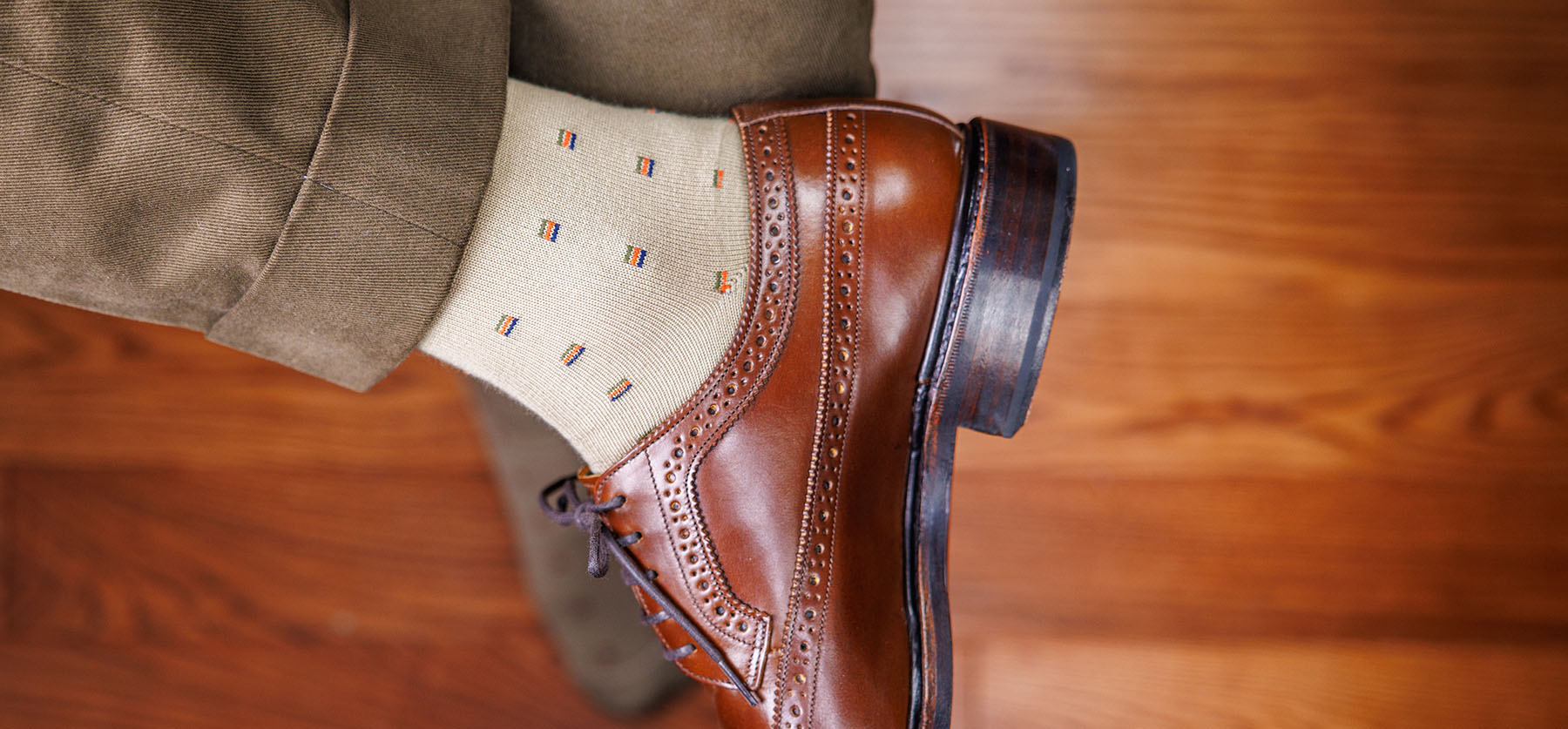 man wearing khaki dress socks with polished brown dress shoes and dark khaki slacks crossing legs