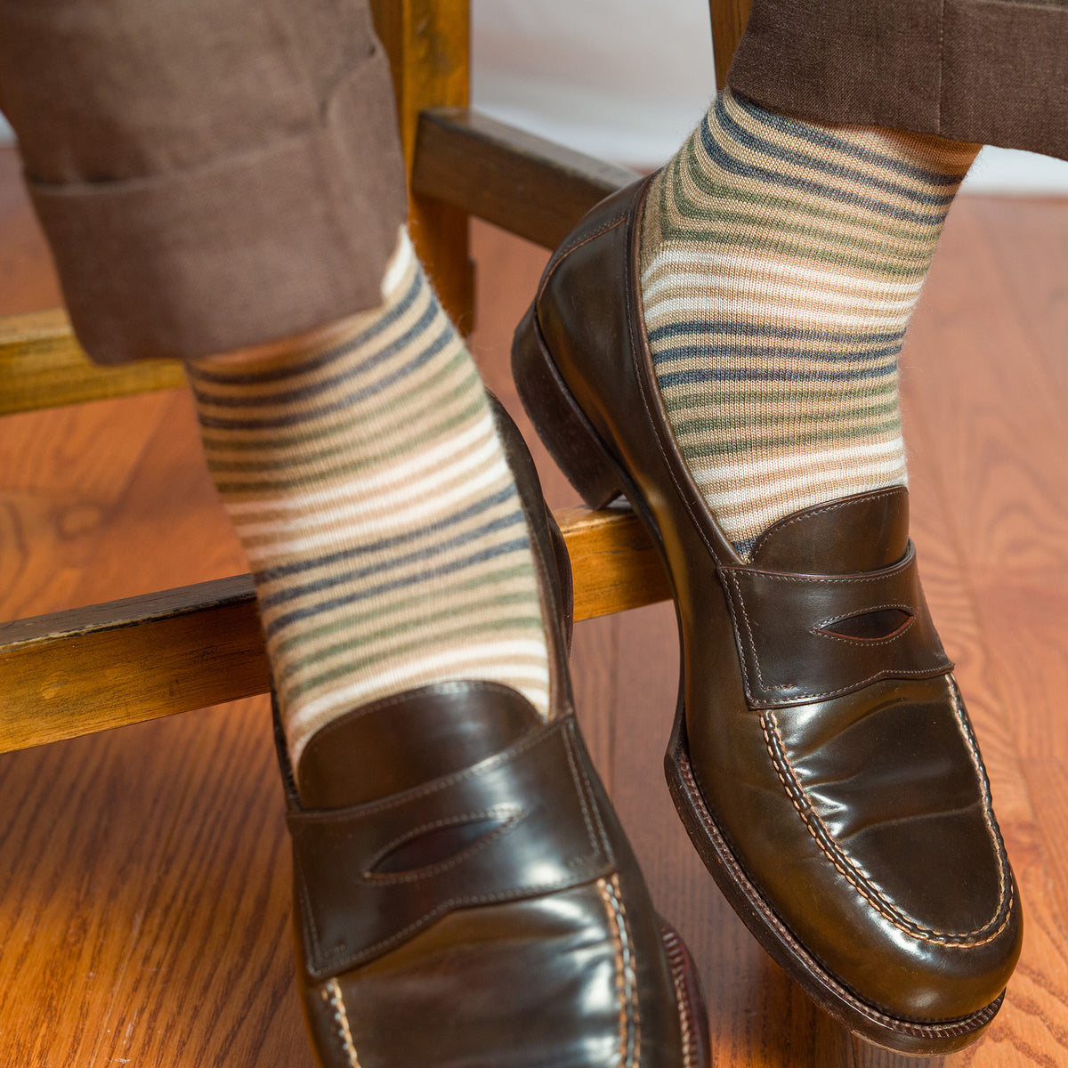 man seated on stool wearing tan striped dress socks with brown slacks and brown penny loafers