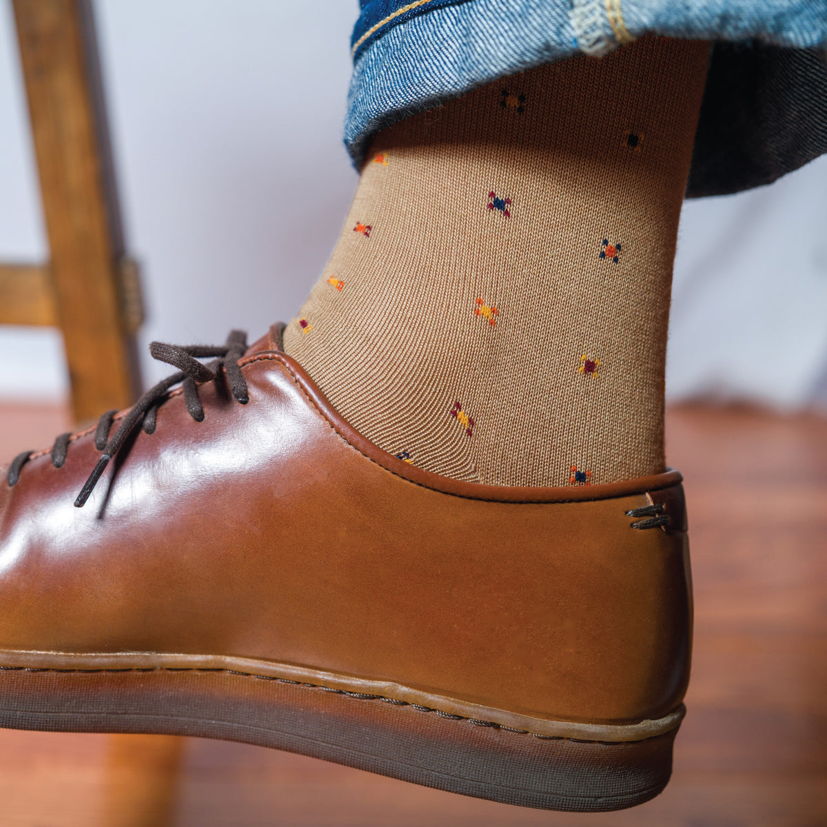 man's right foot held up off of the floor wearing brown lace up. shoes and a pair of khaki geometric pattern cotton dress socks