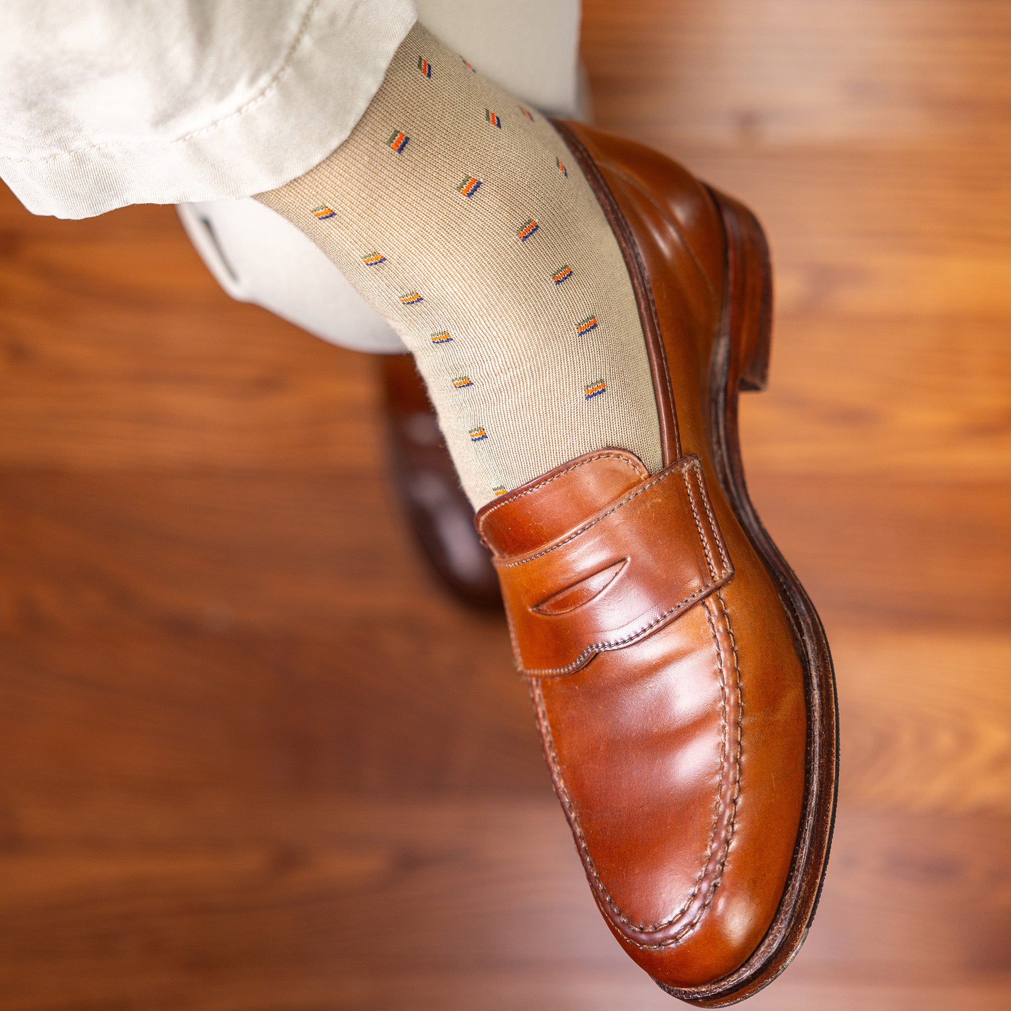 man crossing legs wearing khaki patterned dress socks with brown penny loafers and khakis