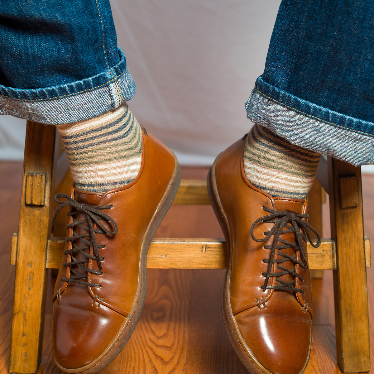 man seated on stool wearing khaki striped dress socks with jeans and brown leather sneakers