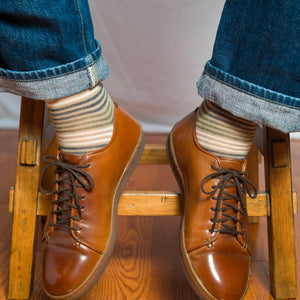 man seated on stool wearing khaki striped dress socks with jeans and brown leather sneakers