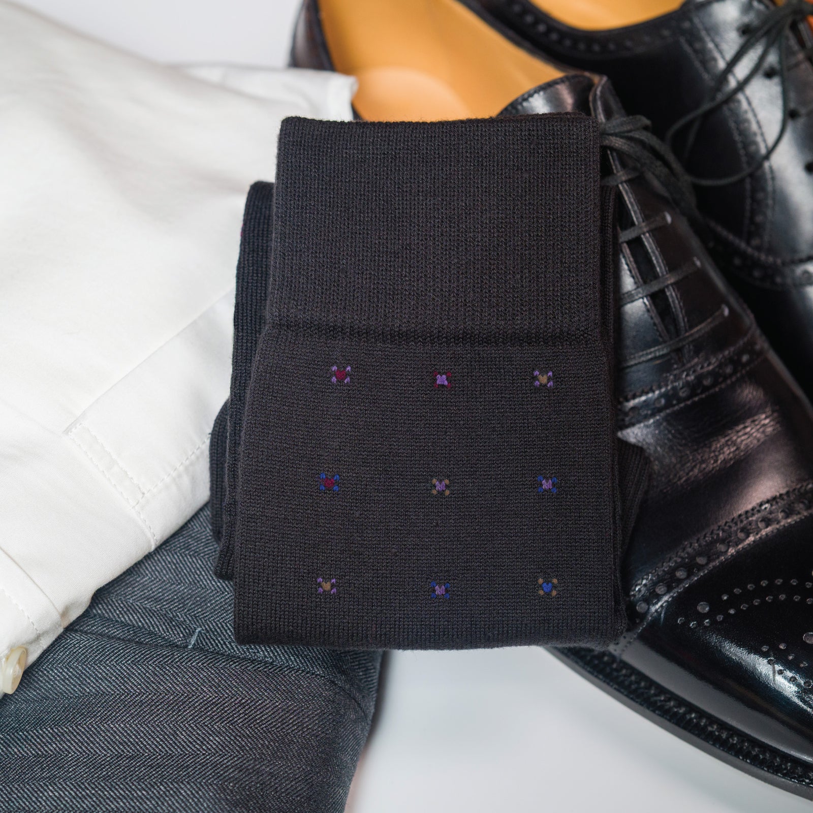 pair of Black Geometric Merino Wool Over the Calf Dress Socks laying on clothing and shoes