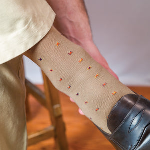 man putting on a brown loafer wearing khaki mid calf length geometric pattern cotton dress socks