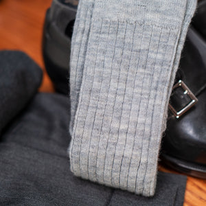 pair of light grey merino wool dress socks resting atop black dress shoes and grey slacks