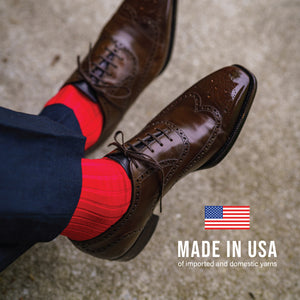 man crossing legs wearing navy slacks, brown dress shoes and red merino wool dress socks 