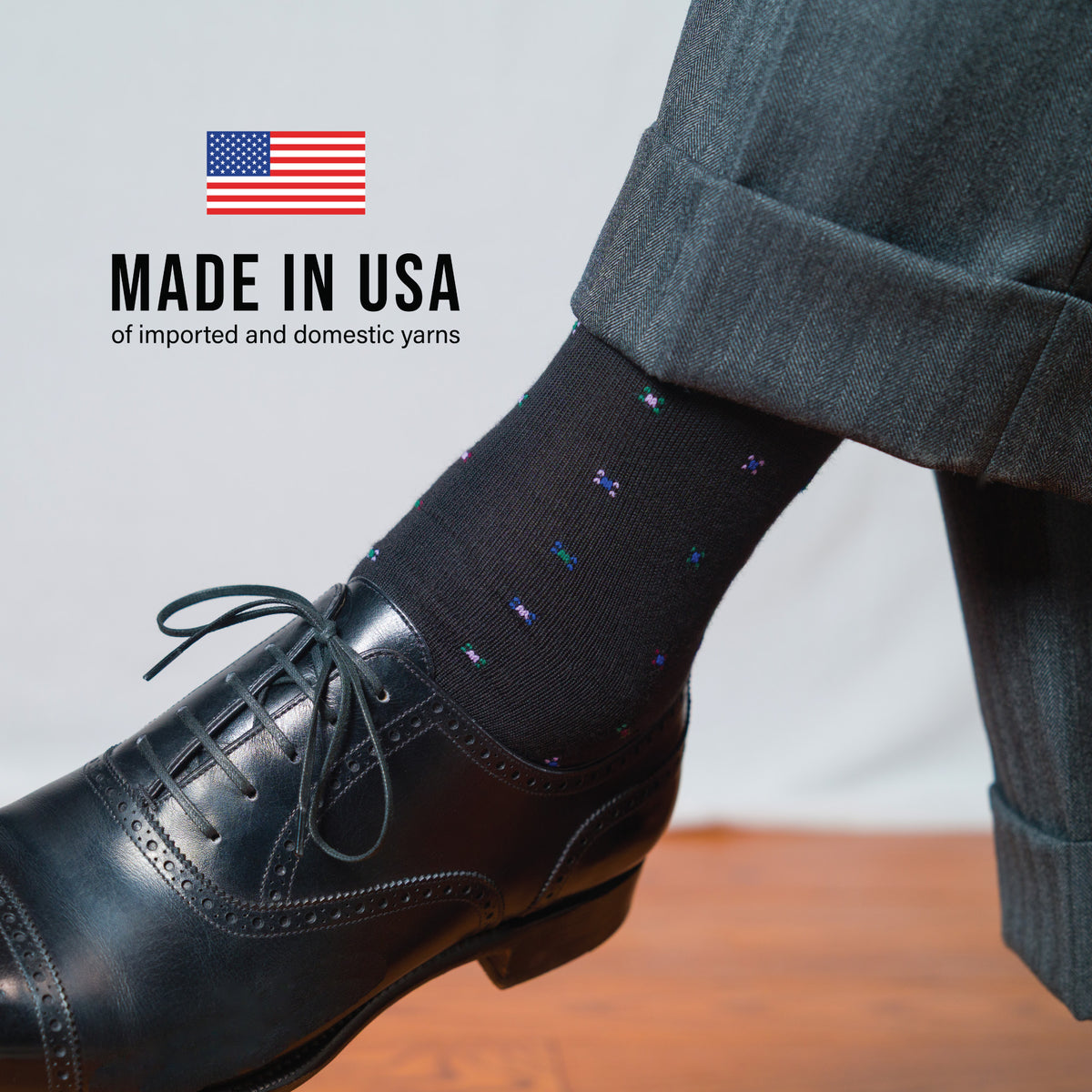 man crossing his legs wearing grey slacks, black oxfords and black geometric cotton dress socks