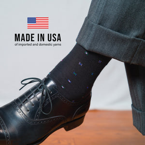 man crossing his legs wearing grey slacks, black oxfords and black geometric cotton dress socks
