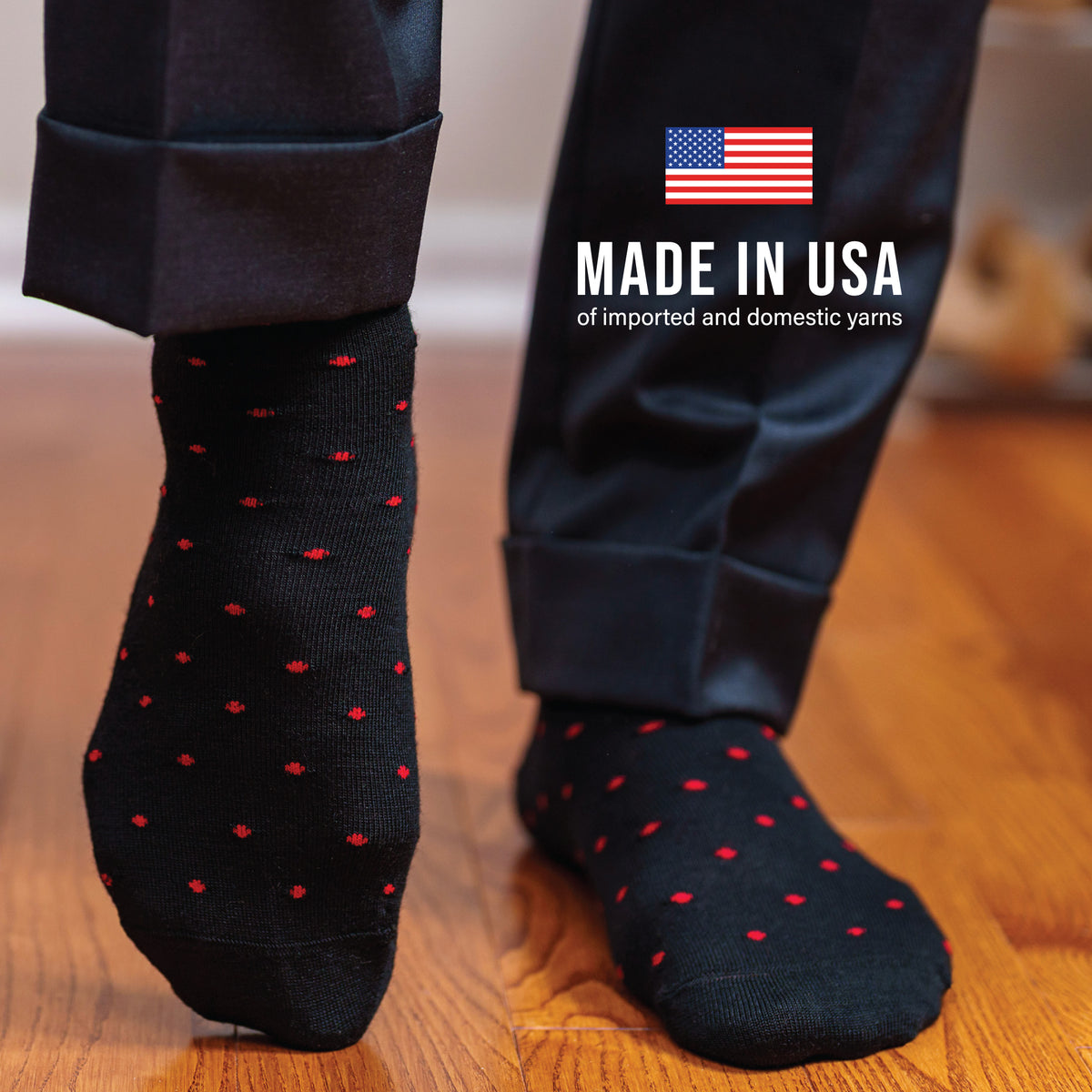man standing on a hardwood floor wearing black merino wool dress socks with a red dot pattern