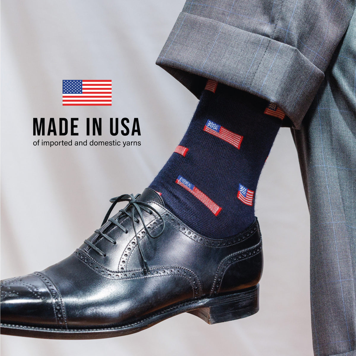 man wearing grey pants, black dress shoes and navy mid-calf merino wool socks with an american flag pattern