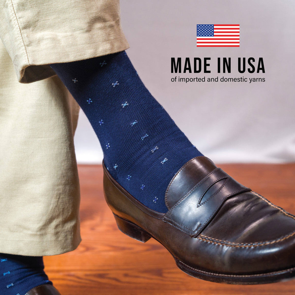 man crossing his legs wearing khakis and navy midcalf geometric pattern cotton dress socks with made in usa text overlay