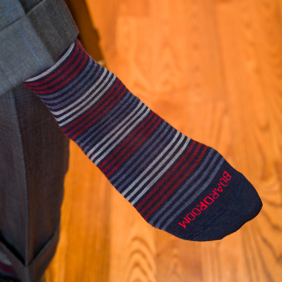 man crossing legs wearing colorful striped navy dress socks with Boardroom stitched across toe in red