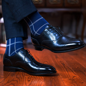 man crossing legs wearing navy suit and windowpane dress socks with black oxfords