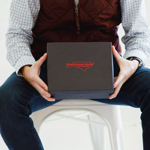man seated holding black box with red embossed Boardroom Socks logo