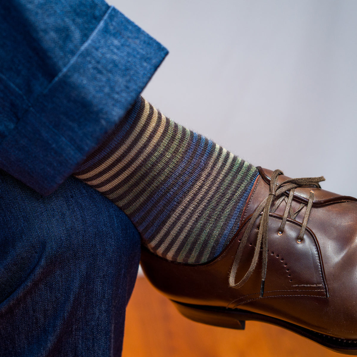 man crossing legs wearing brown striped dress socks with brown dress shoes and navy blue slacks