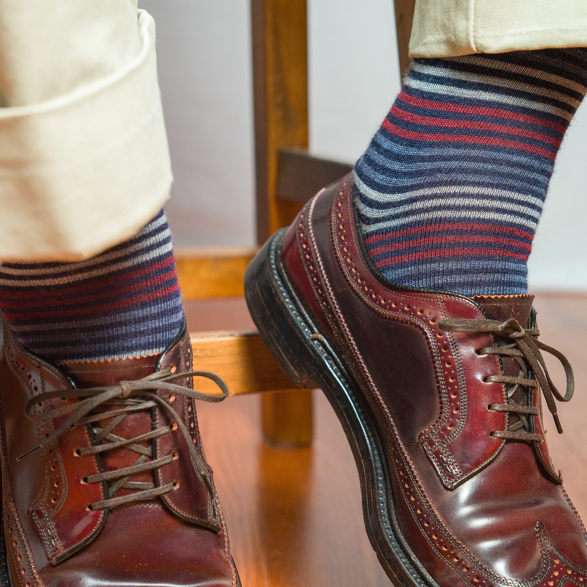 Close-up of colorful striped dress socks worn with brown wingtips and khakis by a man sitting on a stool