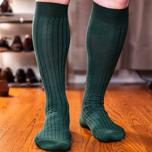 man standing on hardwood floor wearing forest green over the calf socks