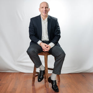 man sitting on a stool wearing nice clothes and light grey heather merino wool dress socks