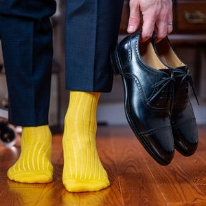 man wearing yellow cotton dress socks and navy suit while holding black oxfords