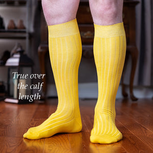 man wearing yellow over the calf dress socks standing on hardwood floor