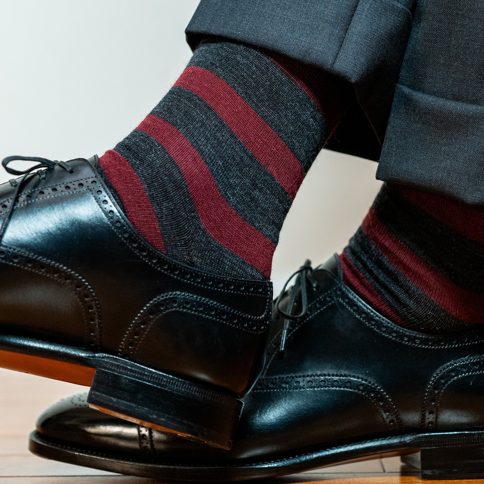 man wearing burgundy and charcoal striped dress socks with black oxfords crossing ankles