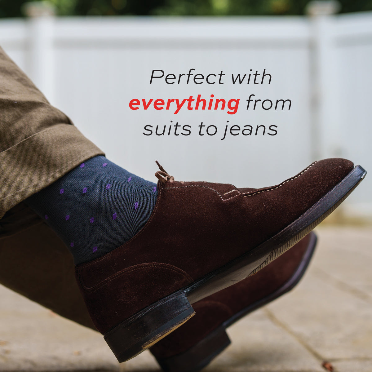 man crossing legs wearing khakis, brown shoes and mid-calf length grey cotton dress socks with purple polka dots
