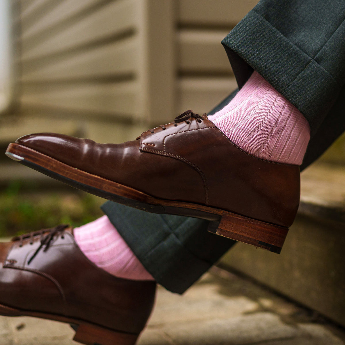 man sitting on stairs and crossing his legs wearing pink merino wool dress socks 