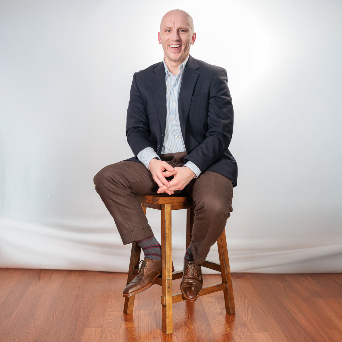 man sitting on a stool wearing Burgundy and Navy Stripes on Grey Merino Wool Over the Calf Dress Socks