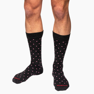 model wearing mid-calf length charcoal dress socks decorated with bright pink polka dots