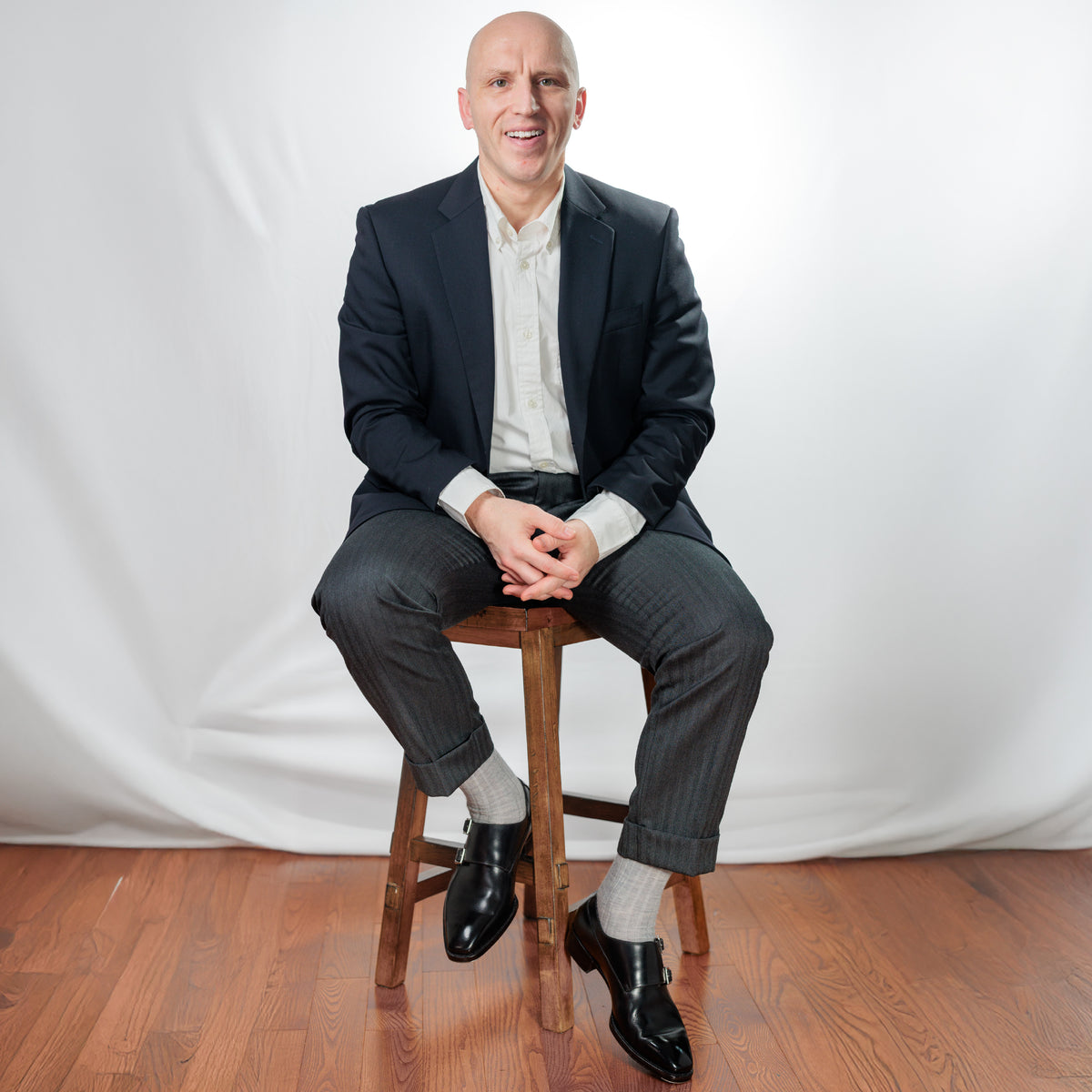 man sitting on a stool wearing nice clothing and light grey merino wool over the calf dress socks