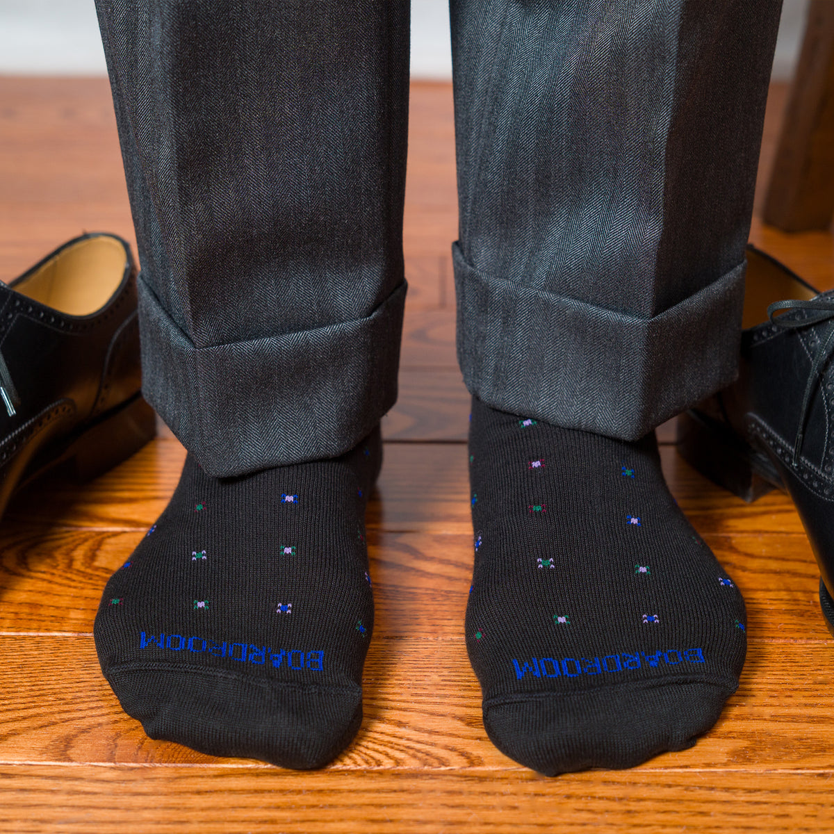 man standing on hardwood floors wearing black cotton dress socks with a geometric pattern