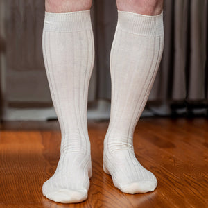 man standing on hardwood floor wearing natural merino wool over the calf dress socks