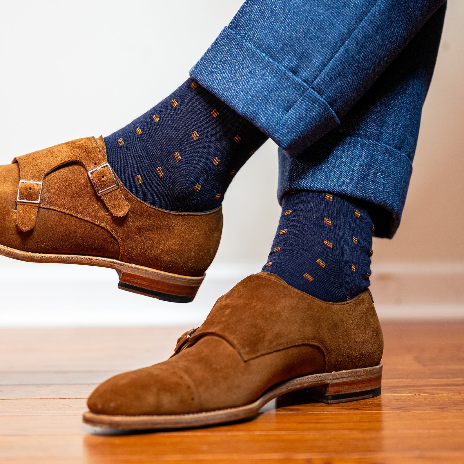 man crossing legs wearing orange and navy dress socks with light blue slacks and brown suede shoes