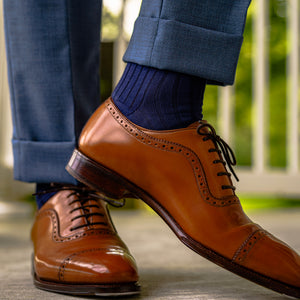 man standing pointing toe to show navy ribbed dress socks and light brown walnut oxfords