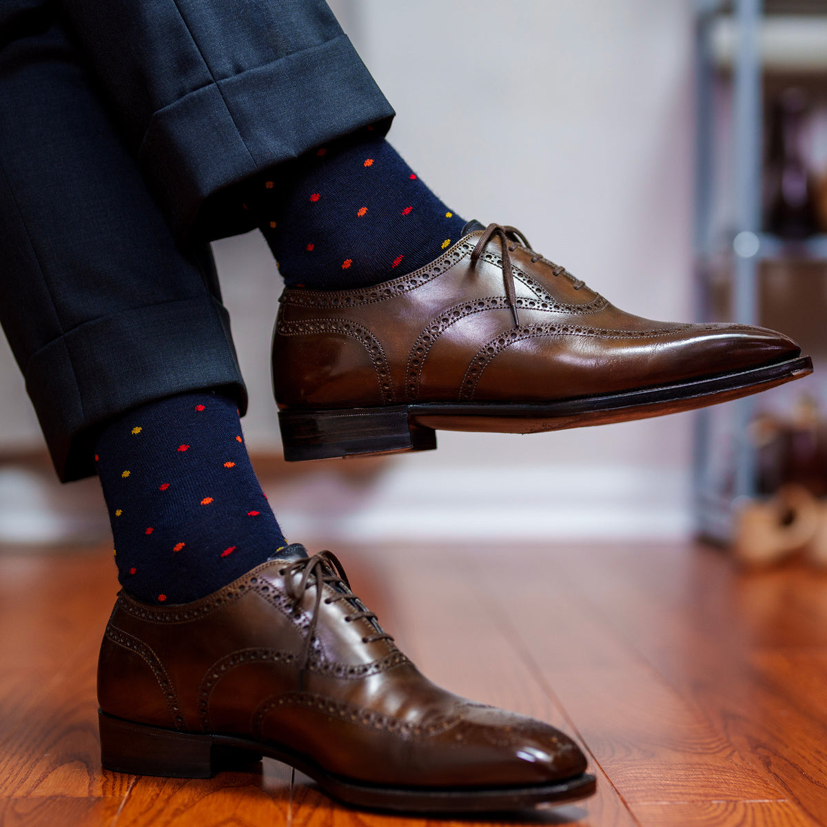 man crossing legs wearing navy dress socks with colorful polka dots and dark brown wingtips