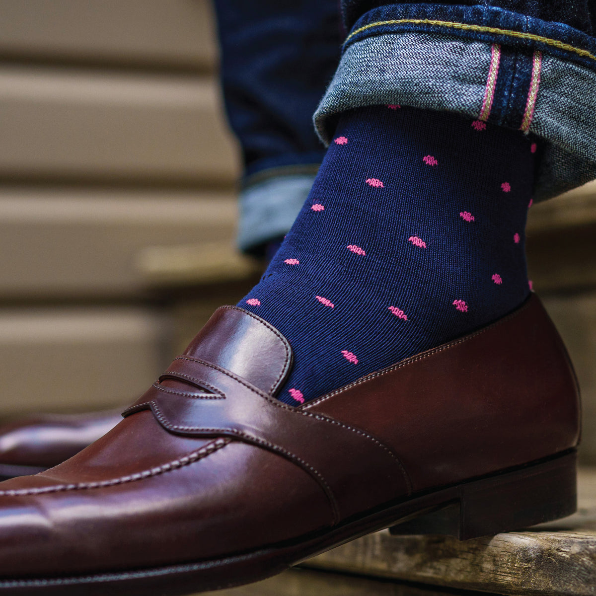 close up of a person wearing jeans and navy mid-calf dress socks with bright pink dots